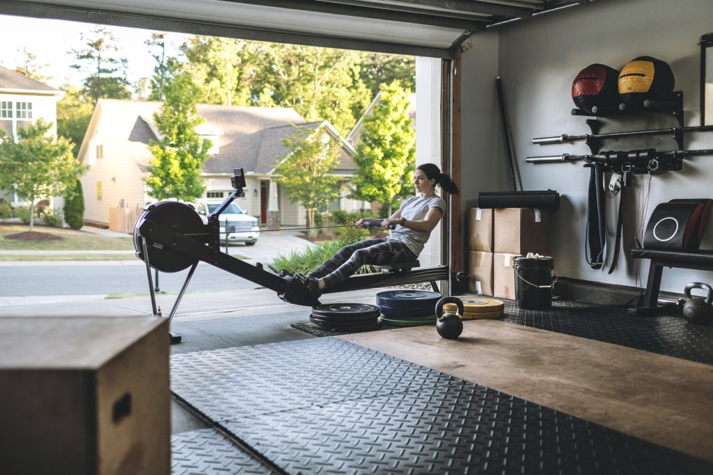 Active woman exercising on a rowing machine in her home garage gym during covid-19 pandemic.