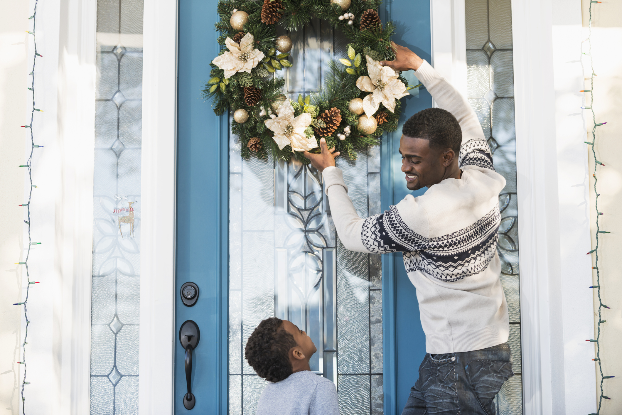 African American father and son hanging wreath on front door